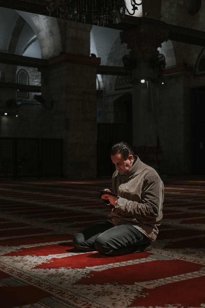 A man kneels in contemplation inside a historic mosque with beautiful architecture.
